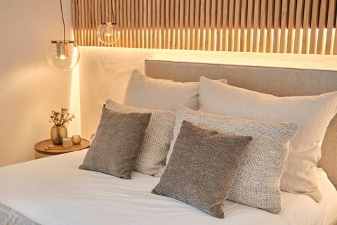 Modern bedroom featuring textured pillows, soft bedding, and ambient lighting with a wooden