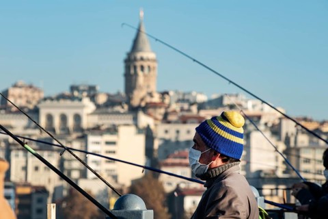 Istanbul, Turkey. November 28th 2020 A man wearing a facemask fishing from the Galata Bridge in