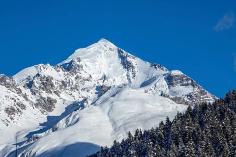 A stunning snow-covered mountain peak stands majestically against a backdrop of a clear, deep blue