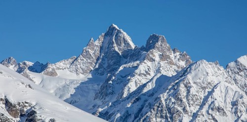 Majestic snow-covered mountain peaks rise against a clear blue sky, capturing the breathtaking