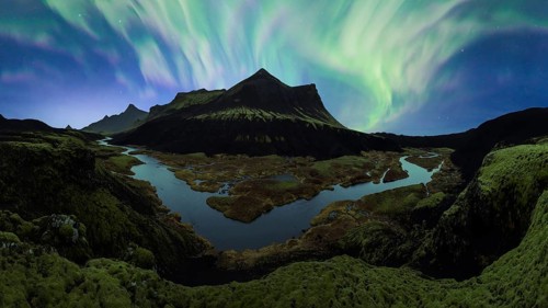 The Northern Lights unfurl in a vibrant dance across the night sky over Iceland's rugged terrain,