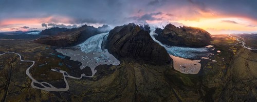 A stunning aerial view of a glacier cascading between volcanic mountains, surrounded by glacial