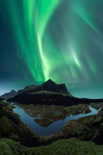 Vivid green Northern Lights dance in the sky above the dark silhouette of Iceland's rugged mountain
