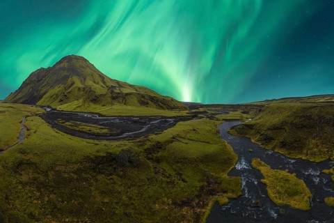 Majestic Northern Lights dance in the sky above a vibrant green valley in Iceland, with a
