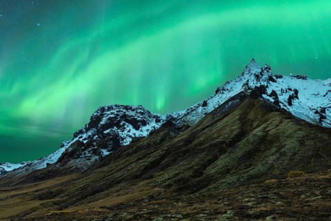 A mesmerizing northern light display dances above snow-capped mountains under a starry Icelandic