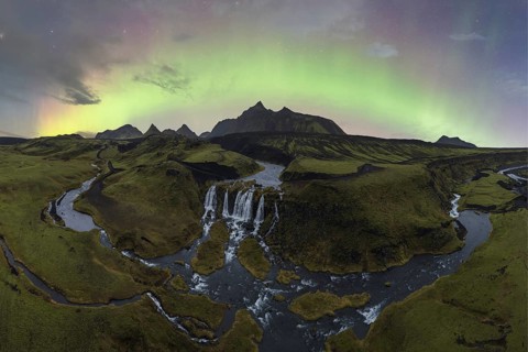 The aurora borealis illuminates the sky above a stunning Icelandic waterfall and meandering river