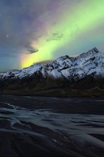Captivating Northern Lights (Aurora Borealis) shine above snow-covered peaks and a riverbed in the