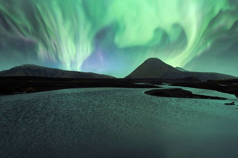 Majestic Northern Lights (Aurora Borealis) illuminate the night sky above a serene Icelandic lake,
