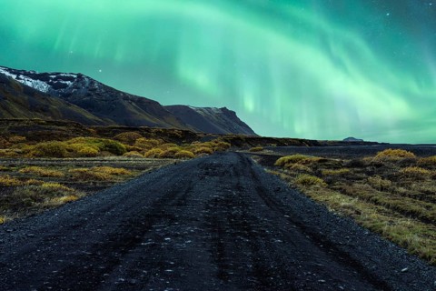 Majestic Northern Lights dancing over a rugged Icelandic landscape with a winding gravel road
