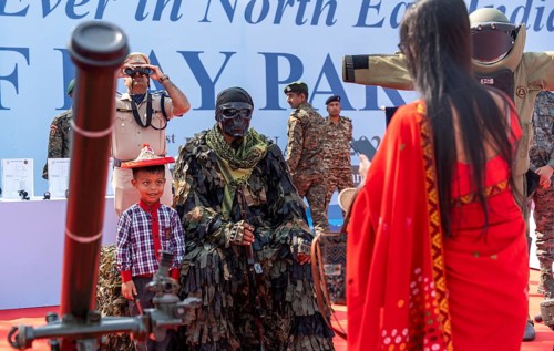 A child poses for a photograph beside a CRPF commando in full camouflage gear during a public