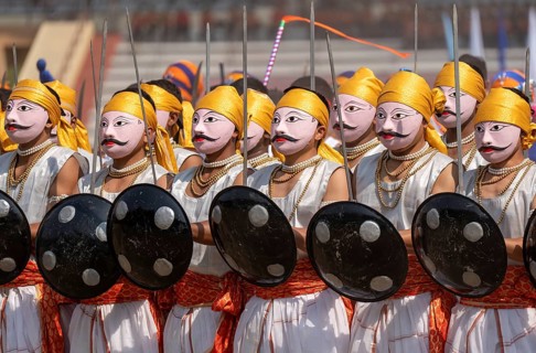 Artists in traditional attire perform a cultural martial dance with swords and shields during the