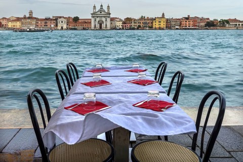 Restaurant tables on the shore in windy weather, on the island of Giudecca, Venice behind, Veneto,