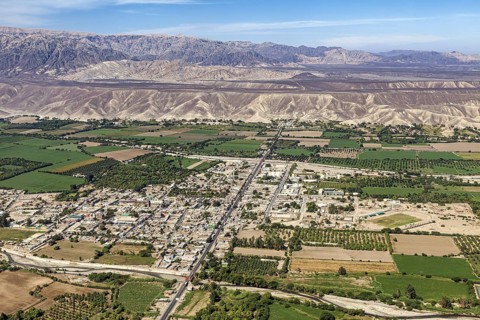 Expansive aerial view of a city with green fields and mountains in the background, The city of