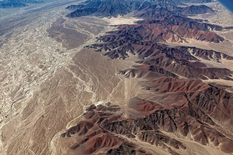 A rugged desert landscape with a series of mountains and a dried-out riverbed, brown and earthy