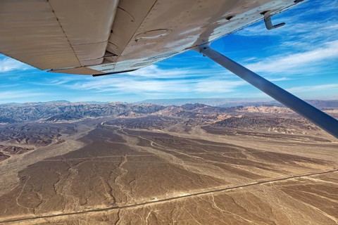 View from an airplane over desert and mountains under a blue sky, the desert landscape near Nasca