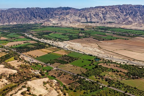 Green fields and river valley in front of a rocky mountain range under clear sky, the desert