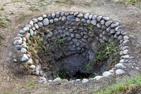 Circular hole in the ground with a rim of stones and some vegetation, The ancient Nazca wells