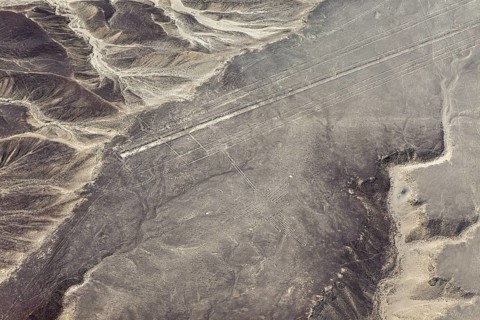 Geoglyphs and lines visible through the air that criss-cross a sandy desert landscape with