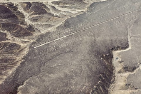 Geoglyph lines in an extensive, sand-colored desert landscape with nearby mountains, the geoglyphs