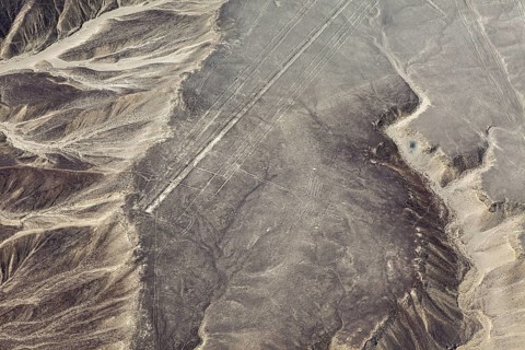 Desert area with linear geoglyph patterns, captured from the air, with mountains in the background,