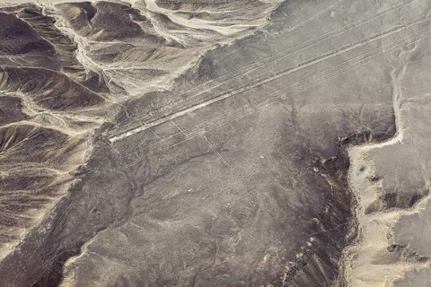 Lines and geoglyphs visible from the air in a desert-like environment surrounded by mountains, The