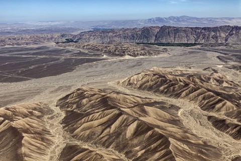 Wide desert landscape with sandy mountains and clear skies that accentuate aridity and vastness,