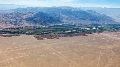An aerial view of a desert landscape with a green oasis and mountains in the background, The