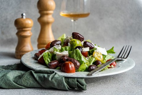 A vibrant Greek salad featuring tomatoes, lettuce, red olives, feta cheese, and olive oil A glass