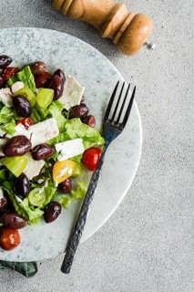 A vibrant Greek salad with tomatoes, lettuce, red olives, and feta cheese Complemented by a pepper