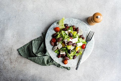 A vibrant Greek salad featuring tomatoes, lettuce, red olives, olive oil, and feta cheese