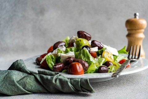 A vibrant Greek salad featuring tomatoes, lettuce, and red olives, topped with feta cheese and