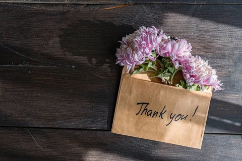 A brown envelope with Thank you written on it holds pink chrysanthemums The flowers rest gracefully