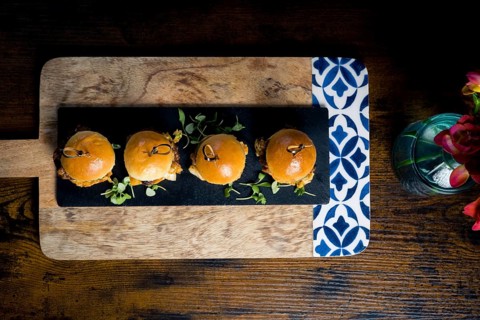 Top-down view of four gourmet pulled pork and cabbage mini burgers served on a black slate board