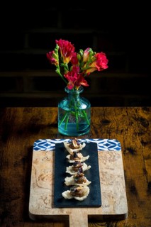 Elegant cracker canapes topped with vegetable satay stew and peanuts, served on a black slate over