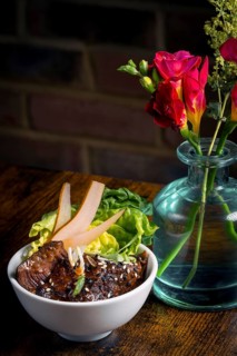 A beautifully presented Asian beef bowl garnished with fresh greens and pear slices, paired with a