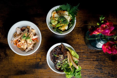 Top-down view of three gourmet bowls, broccoli and cauliflower in satay sauce, chicken with glass