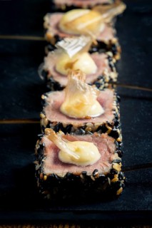 Close-up of rare tuna steaks coated in sesame seeds, topped with mayonnaise and garnished with