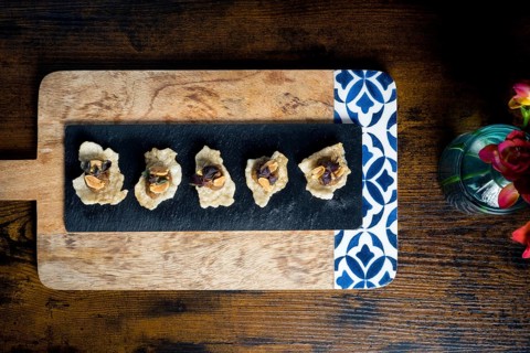 Crispy cracker canapes topped with vegetable satay stew and peanuts, arranged on a black slate over