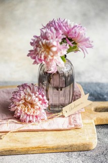 Elegant chrysanthemums in a textured glass vase, set on a wooden board, create an autumnal theme A