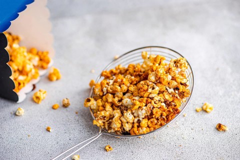 Top view of sweet caramel popcorn served in a transparent bowl on a textured gray background. The