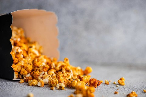 Caramel popcorn tumbling out of a black carton onto a textured gray background