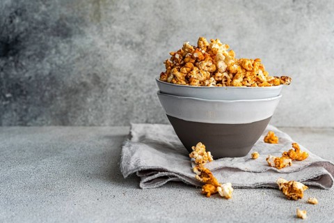 Gray bowl overflowing with sweet caramel popcorn is set on a textured linen, against a textured