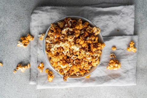 Top view of a bowl filled with sweet caramel popcorn, garnished with scattered pieces on grey