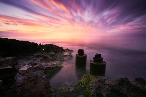 A mesmerizing sunset with vibrant hues reflecting over calm waters, coastal rocks, and ancient