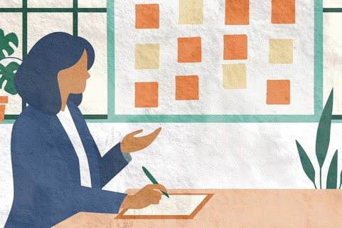 A businesswoman is seated at a table, writing notes while gesturing towards a wall covered with