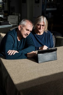 A senior couple sits at a table in a cozy living room, engaged with a digital tablet They appear to