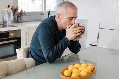 A senior man enjoys a warm cup of coffee at a glass table in a modern kitchen A bowl of lemons