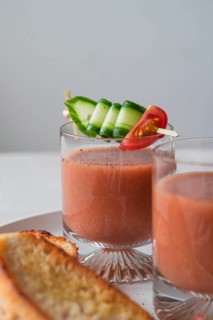Clear glasses of gazpacho garnished with cucumber and tomato skewers A slice of crispy toast is
