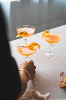 Cropped unrecognizable person holding a glass of vibrant mandarin cocktail, garnished with an