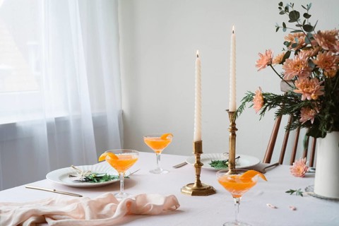 An elegantly set table featuring refreshing Mandarin drinks, lit beeswax candles, intricate floral
